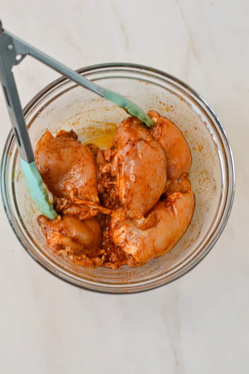 Chicken thighs being tossed in a bowl with the spices for the sheet pan dinner.
