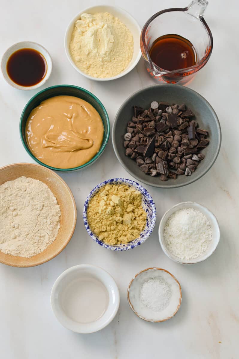 Ingredients for cookie dough balls including oat flour, chocolate chips, vanilla extract. maple syrup, cashew butter, ground flax seed, salt, and protein powder.