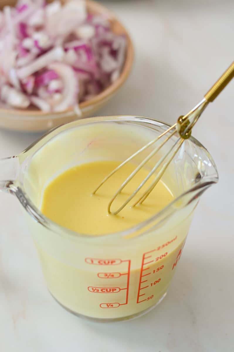 Creamy dijon and honey mustard salad dressing whisked in a measuring glass.