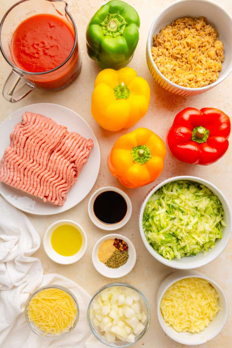 Ingredients to make stuffed peppers including peppers, ground turkey, zucchini, onion, rice spices, olive oil, balsamic vinegar, and tomato sauce.