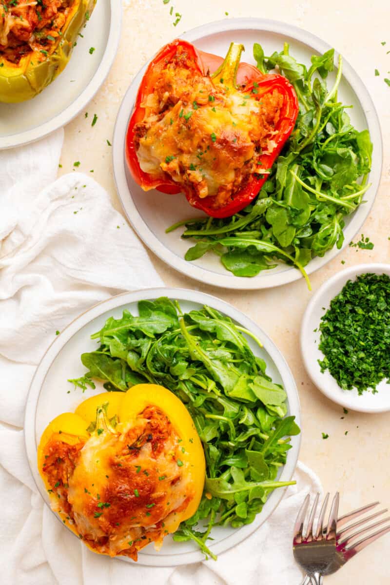 Two plates with ground turkey stuffed peppers paired with a salad.