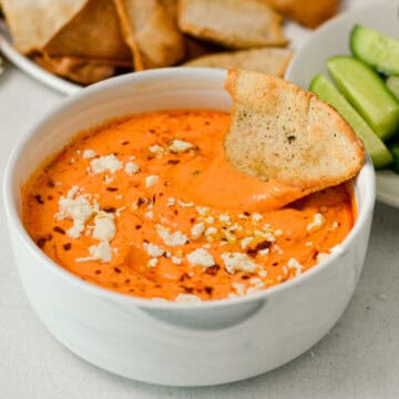 Roasted red pepper dip in a bowl with a pita chip.
