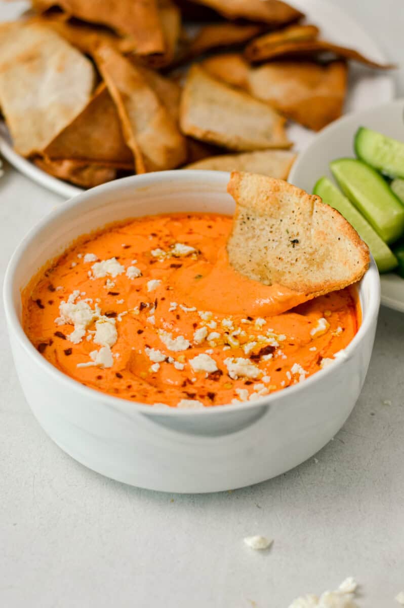 Roasted red pepper dip in a bowl with a pita chip.