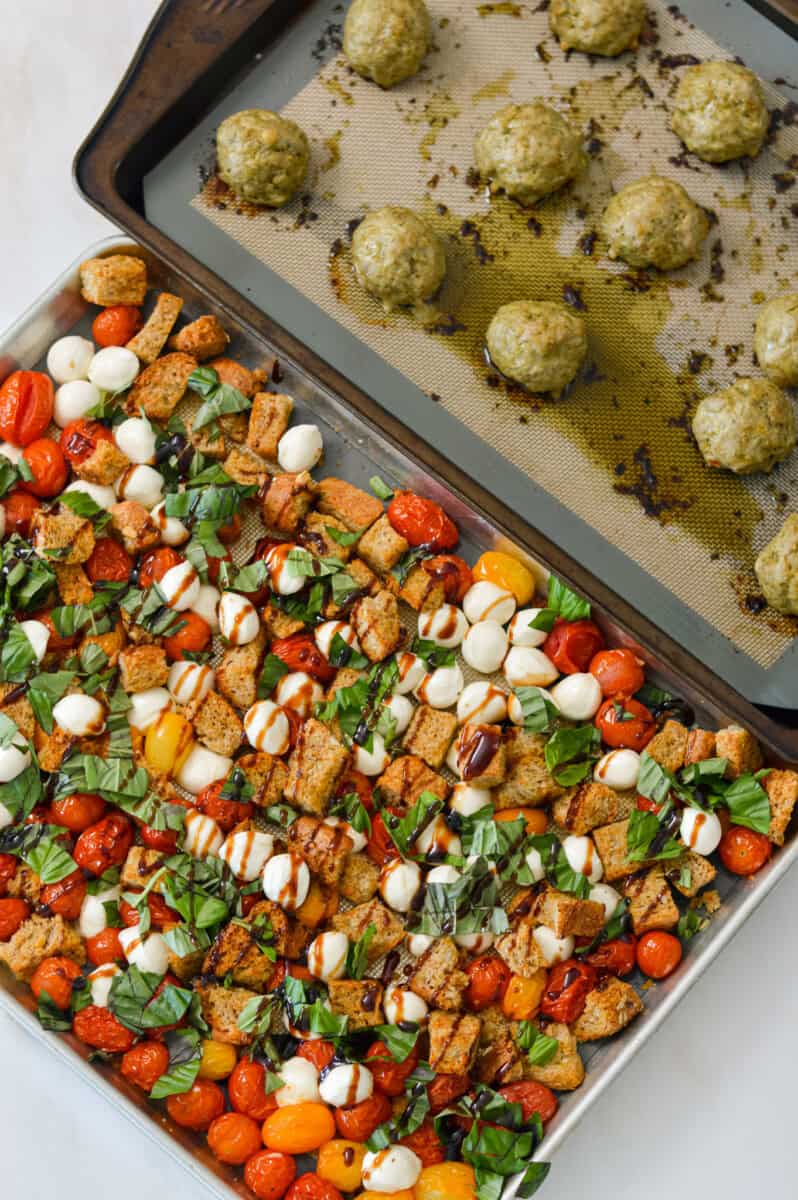Cooked chicken meatballs on a sheet pan with the caprese sheet pan next to it.