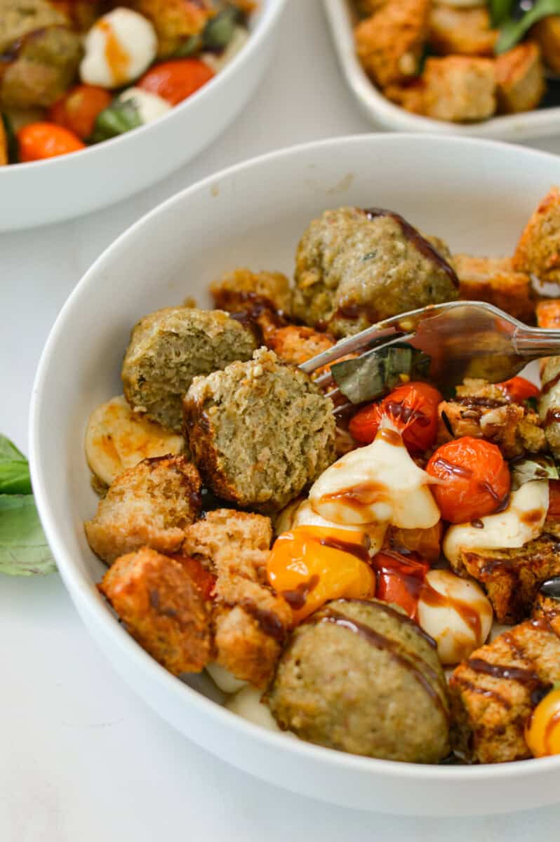 Pesto chicken meatballs and caprese sheet pan added to a bowl.