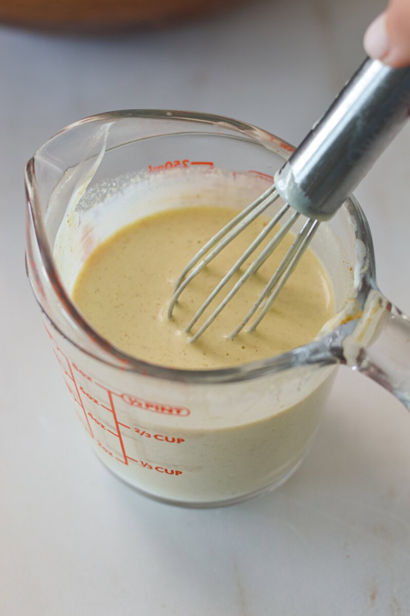 Creamy Dijon, lemon dressing being whisked in a measuring cup.