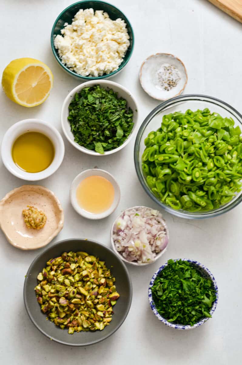 Ingredients for salad including sugar snap peas, feta, pistachios, shallots mint, lemon, olive oil, salt, pepper, honey, and dijon mustard.