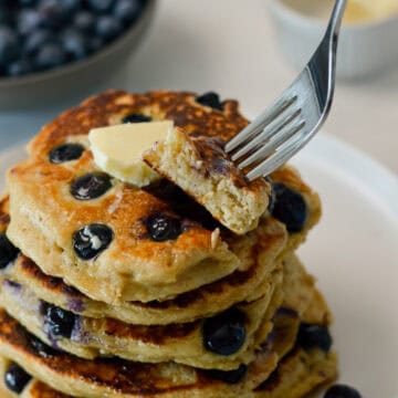 Fork lifting up a bite of a pancake from a stack of pancakes.