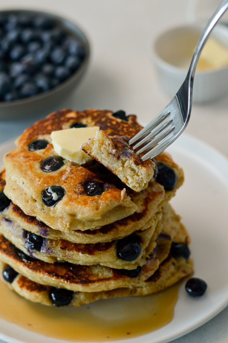 Fork lifting up a bite of a pancake from a stack of pancakes.