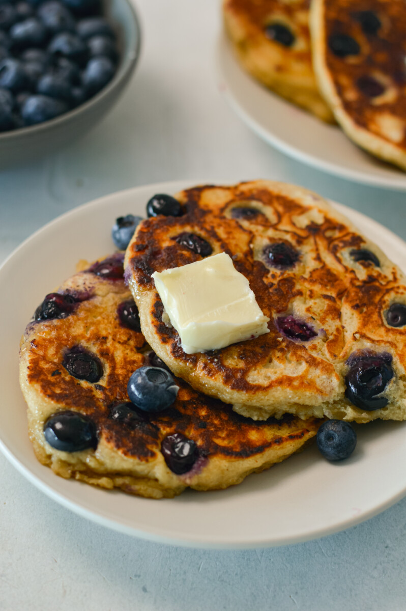 Two blueberry pancakes on a plate topped with butter.