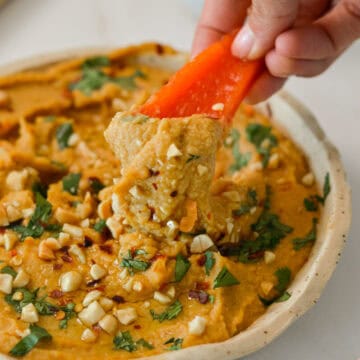 Red pepper scooping up peanut butter hummus out of a bowl.