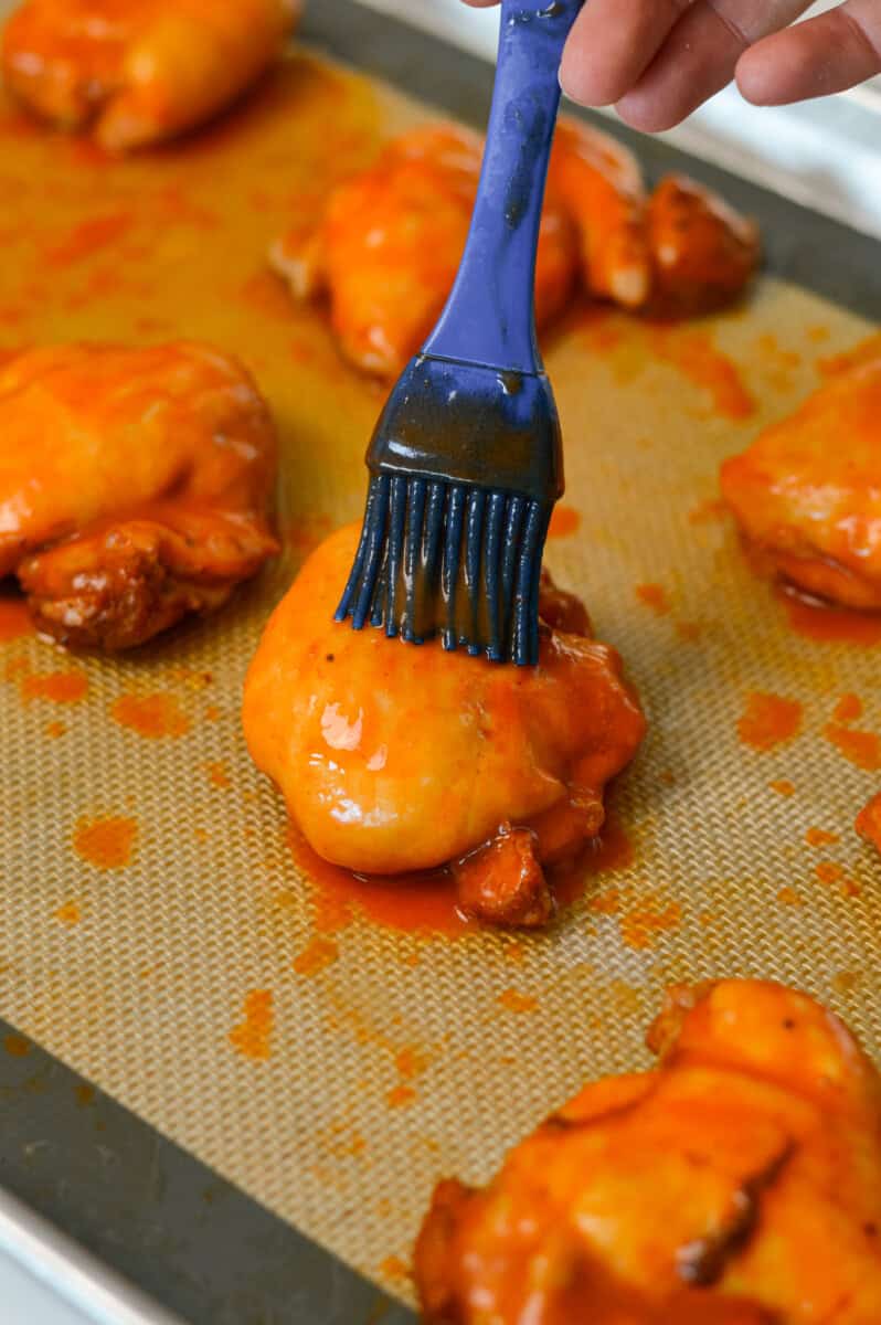 Brushing a chicken thigh with hot honey butter sauce.