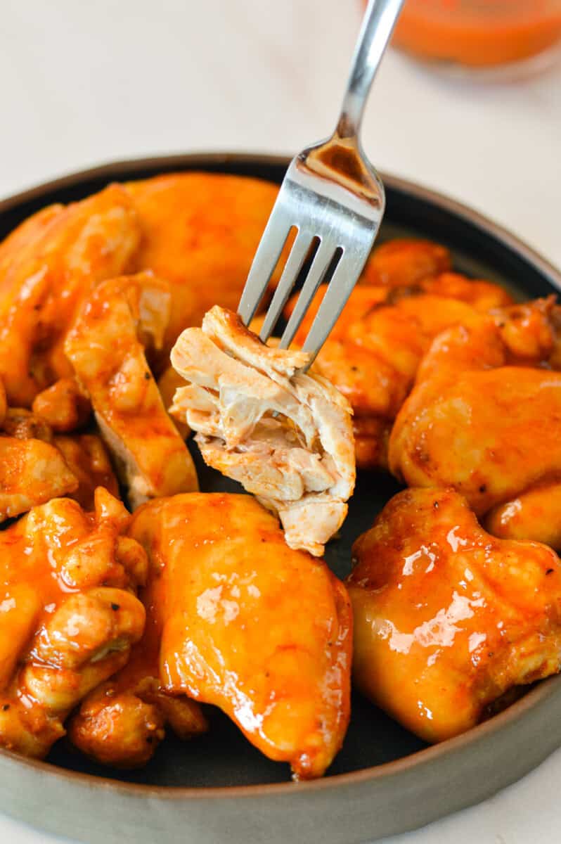 Fork lifting a bite of a chicken thigh.
