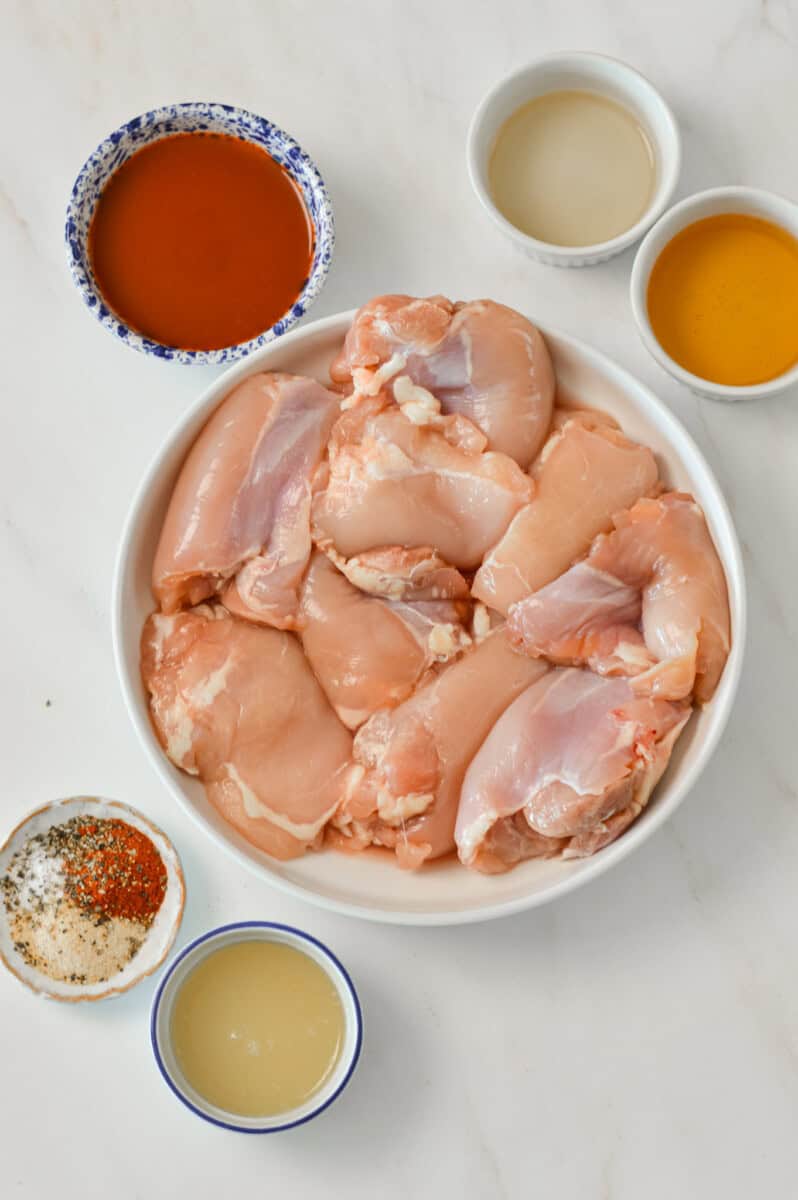 Ingredients for hot honey chicken thighs including chicken thighs, hot sauce, honey, olive oil, and spices.