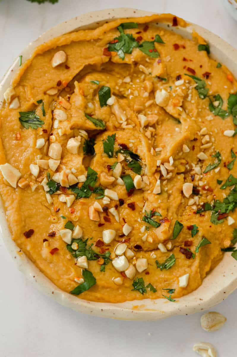 Close up of peanut butter hummus with peanuts, cilantro, red pepper flakes and olive oil drizzle.