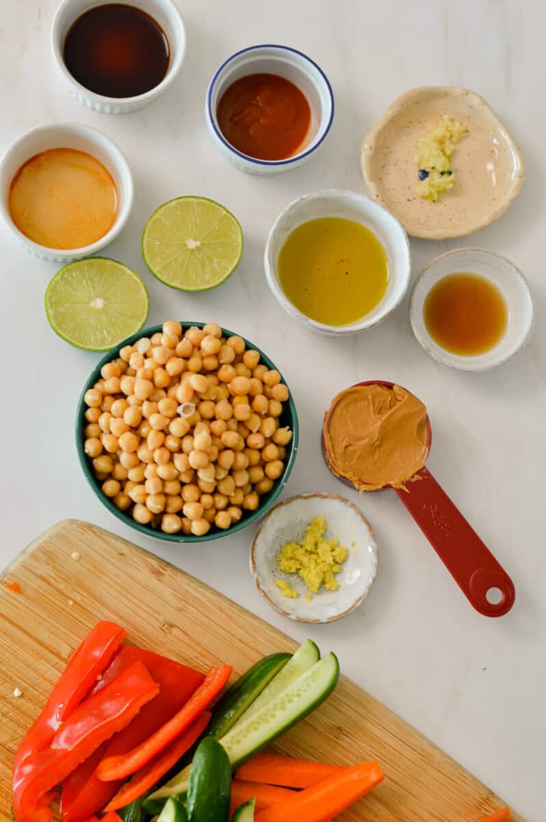 Ingredients for peanut butter hummus including chickpeas, ginger, lime, honey, sriracha, olive oil, fresh garlic, sesame oil and soy sauce.