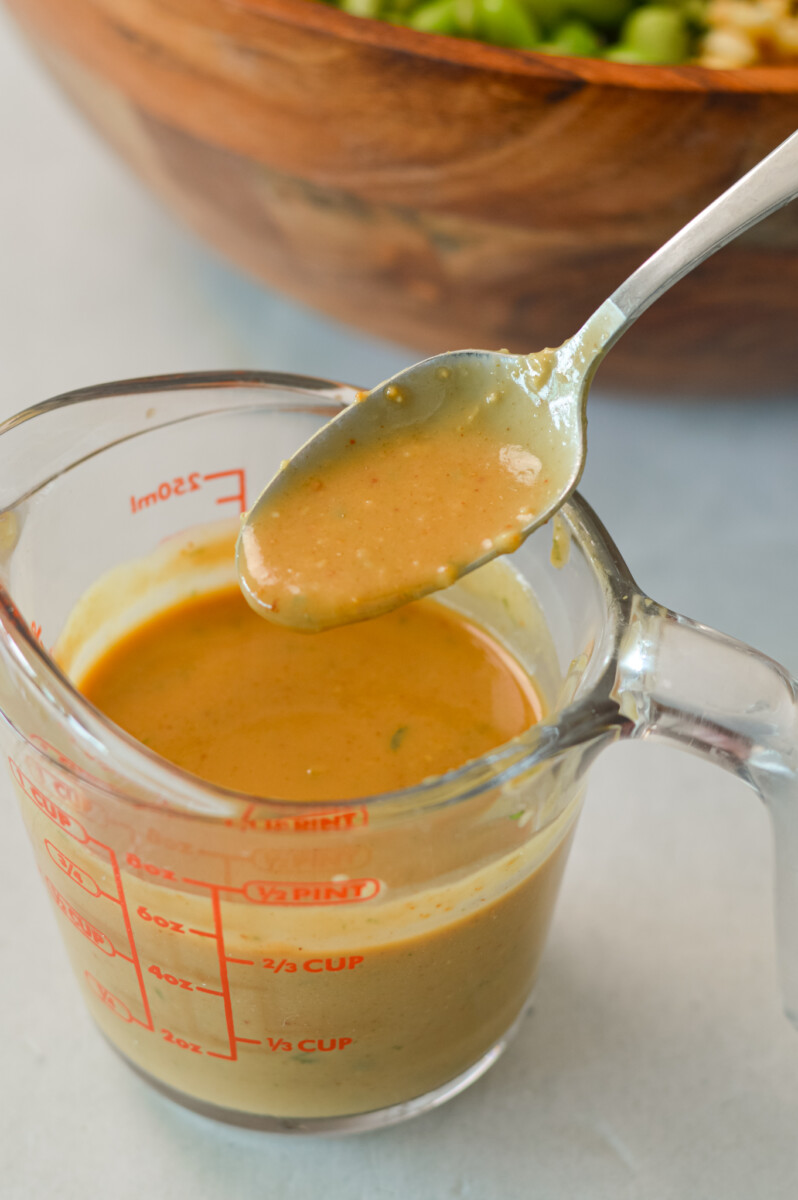 Spoon lifting up creamy peanut dressing out of a measuring cup.