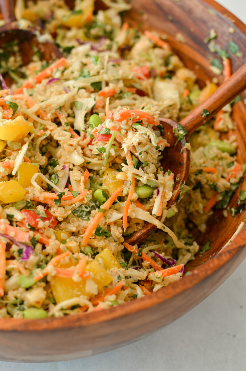 Close up of a salad tong lifting up the peanut quinoa salad out of a salad bowl.
