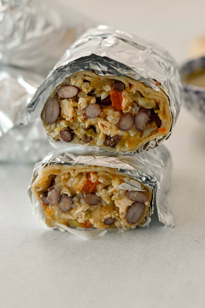 Stack of a finished burrito wrapped in tinfoil, sliced in half.