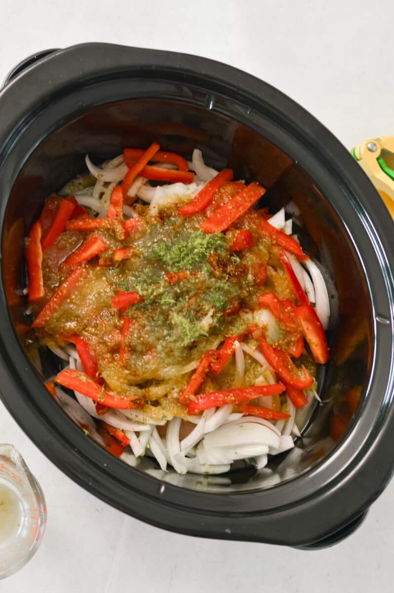 Onions, chicken and peppers added to a slow cooker.