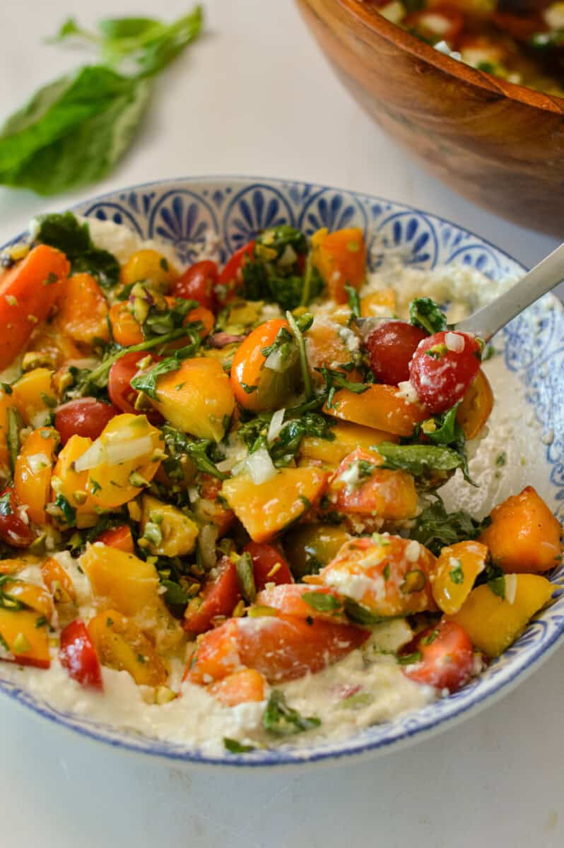 Close up of a spoon lifting a bite of the tomato, peach and burrata salad.