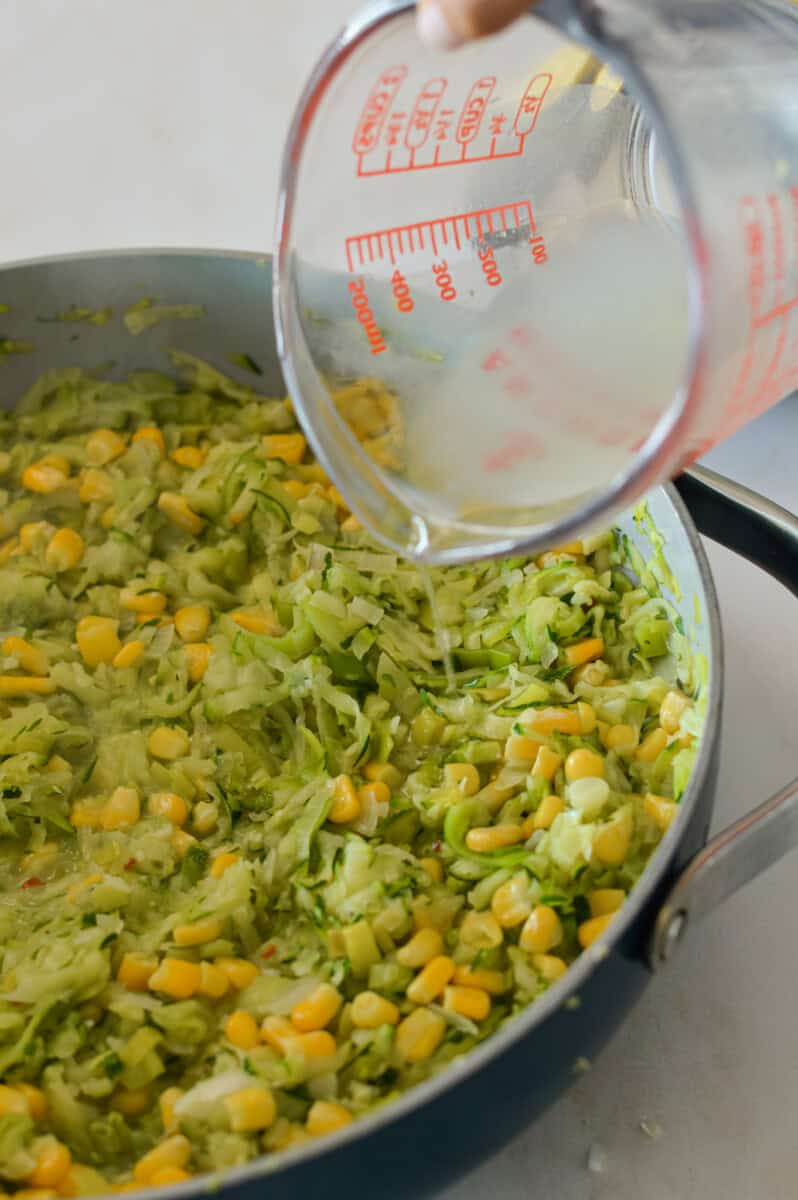 Pasta water being poured into the pan with zucchini, leeks and corn.