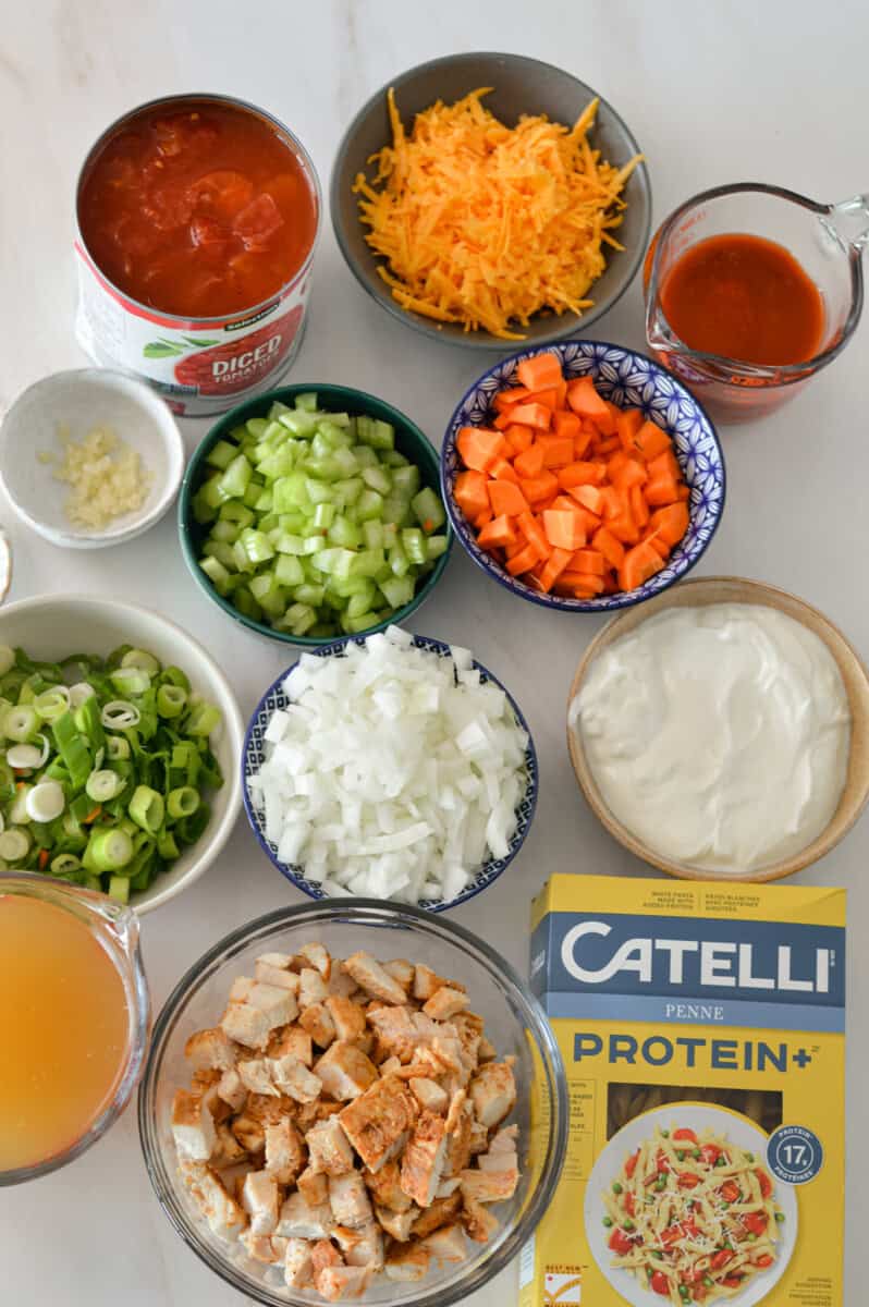 Ingredients for pasta dinner including cooked chicken, protein pasta, buffalo sauce, 5% Greek yogurt, celery, carrot, onion, buffalo sauce, diced tomato, reduced sodium chicken broth, shredded cheddar, green onion, and garlic.