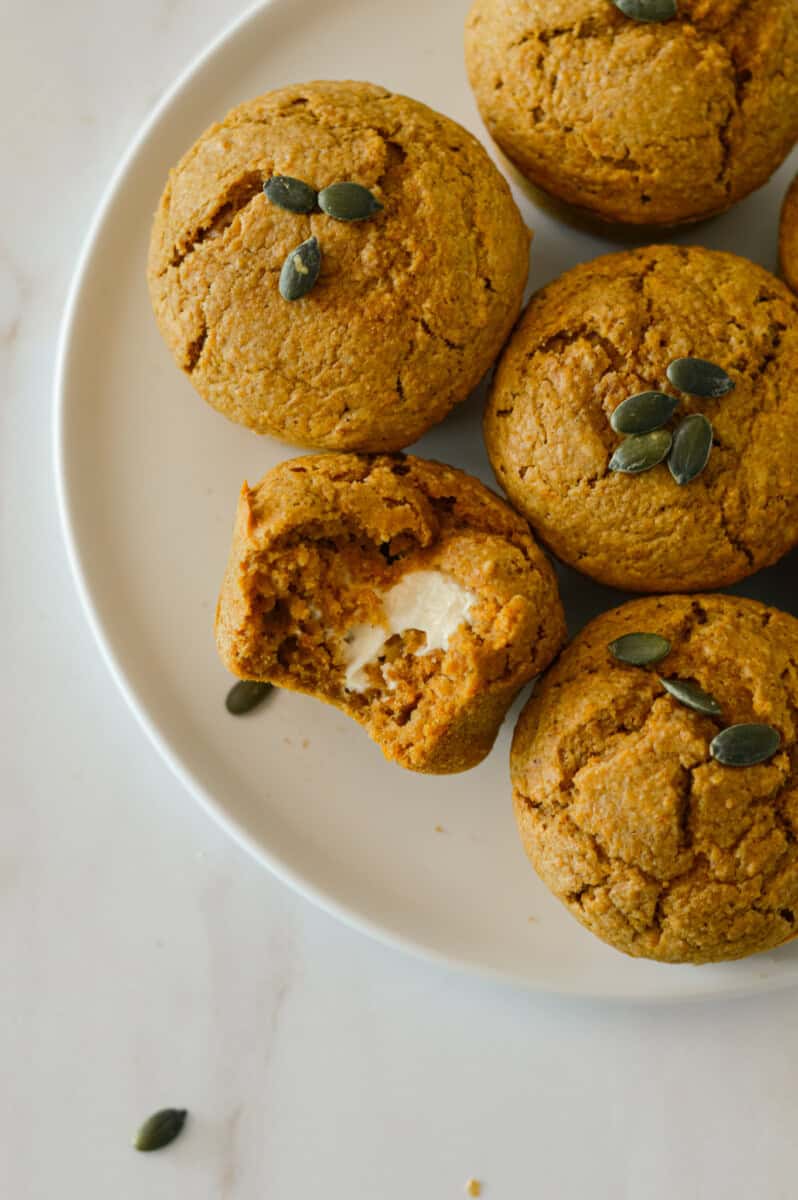 Pumpkin cream cheese muffins on a plate with one having a bite taken out of it.
