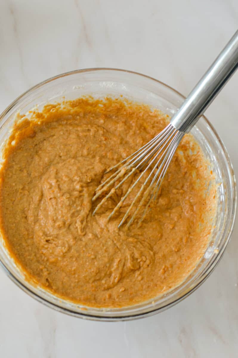 Wet and dry ingredients for pumpkin cream cheese muffins combined in a mixing bowl.