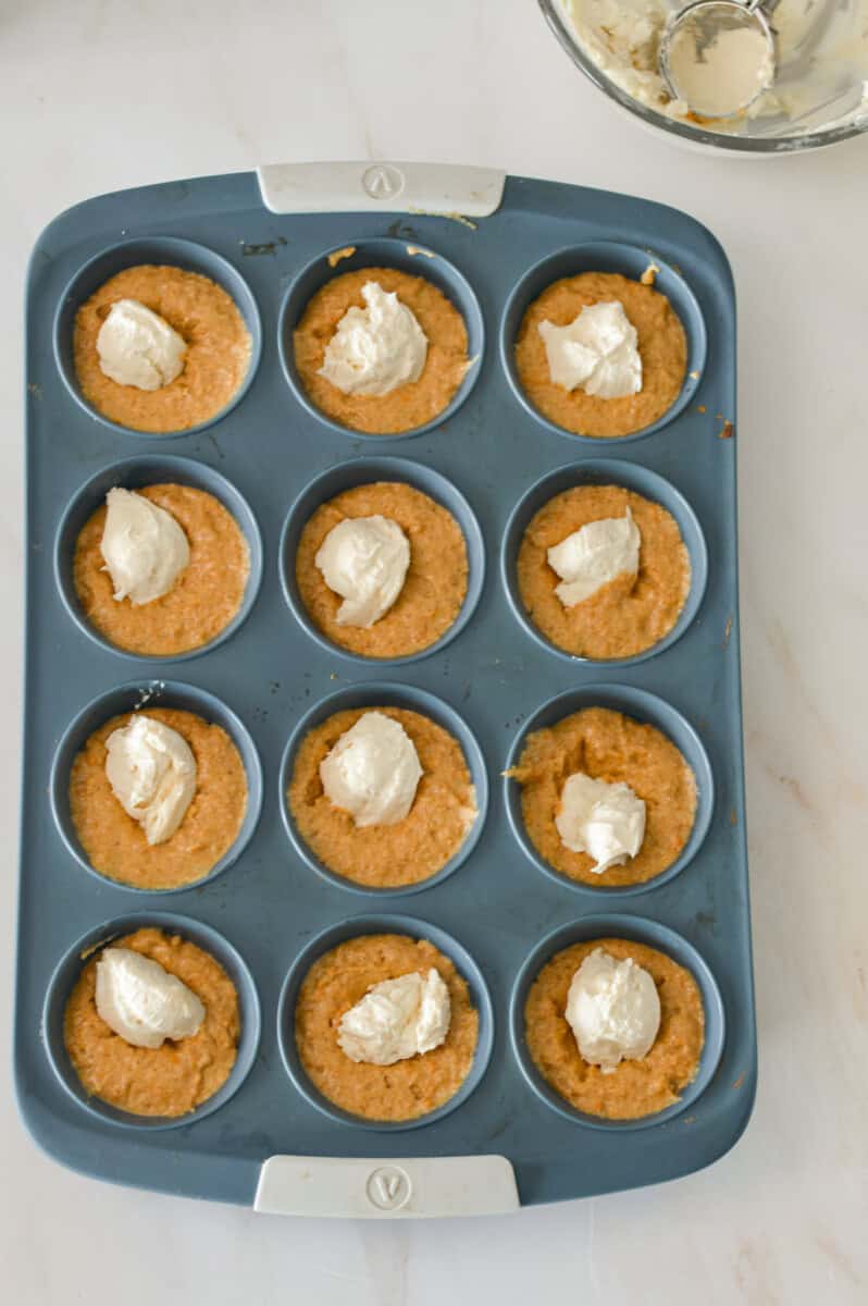 Muffin batter divided in a muffin tray and cream cheese center added.