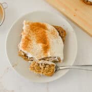 Slice of cinnamon roll baked oats on a plate with a fork cutting into it.