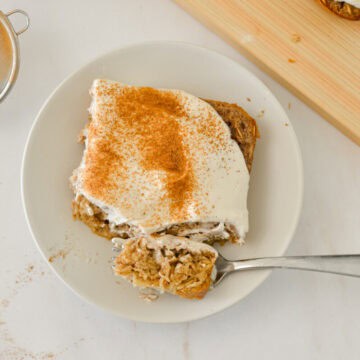 Slice of cinnamon roll baked oats on a plate with a fork cutting into it.