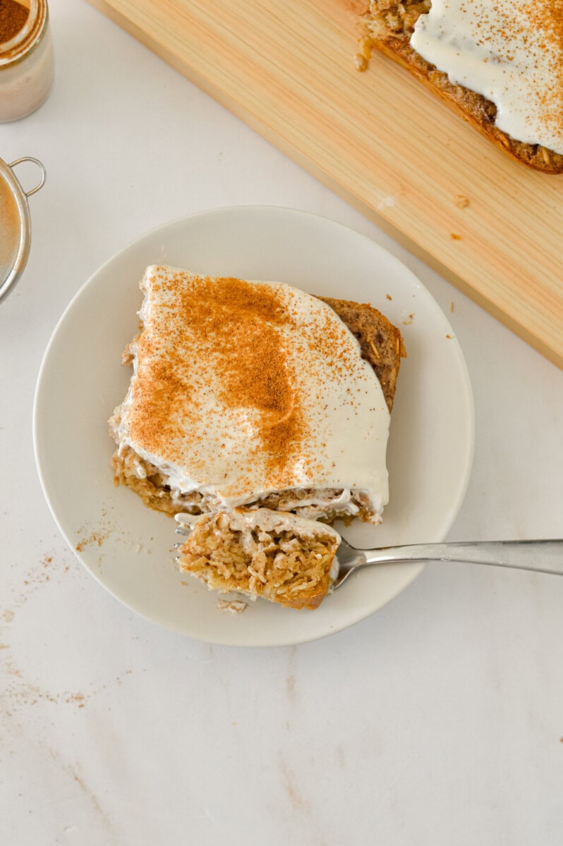 Slice of cinnamon roll baked oats on a plate with a fork cutting into it.