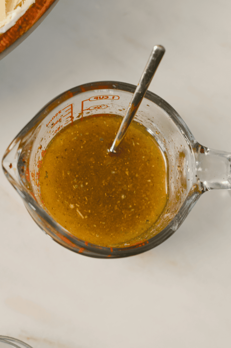 Dijon, olive oil, garlic, oregano, lemon juice, salt and pepper combined in a measuring cup.