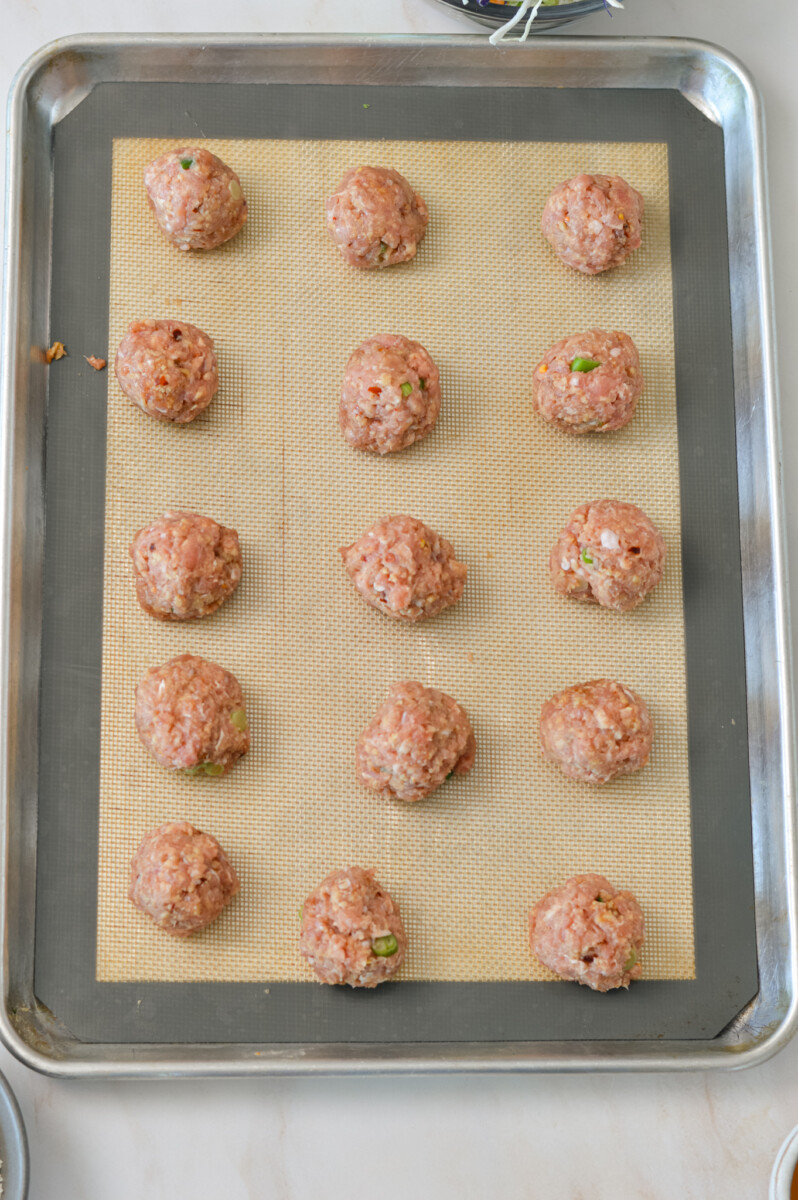 Chicken meatballs rolled out onto a baking tray.