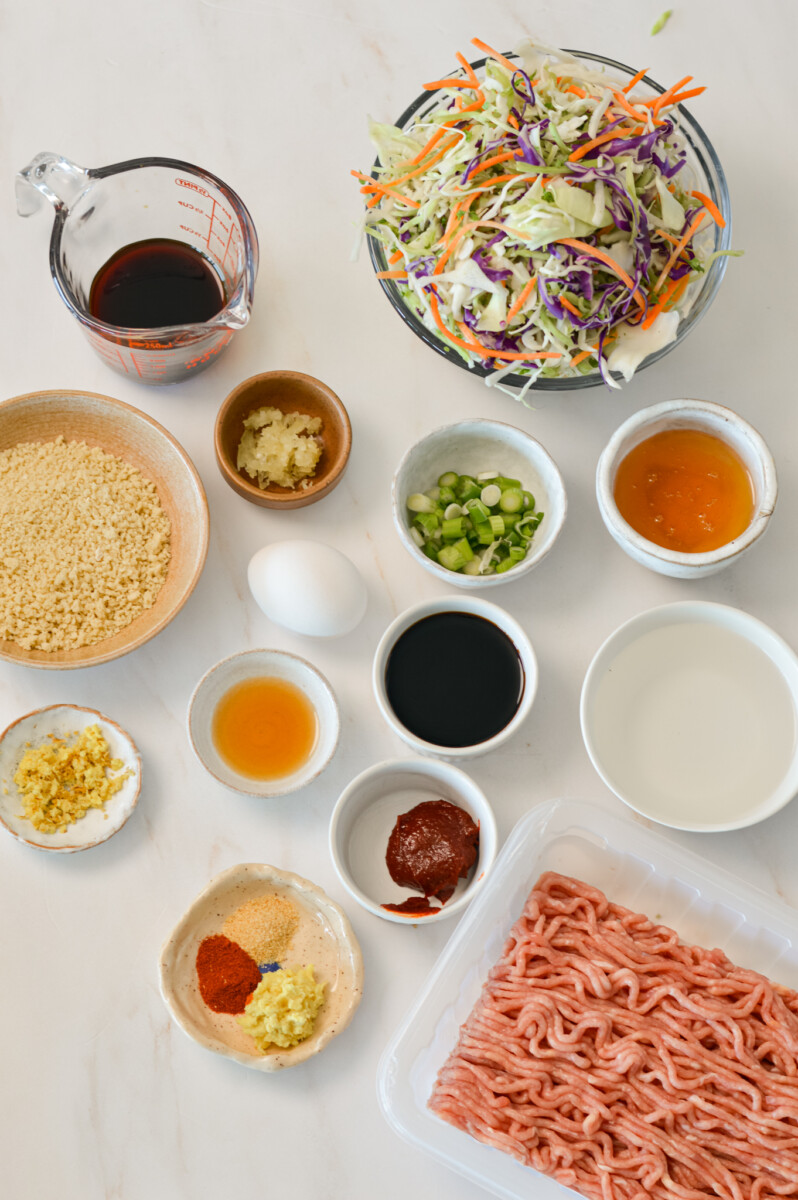 Ingredients for Asian meatball bowls including ground chicken, coleslaw mix, eggs, panko, breadcrumbs, soy sauce, sesame oil, fresh ginger and garlic, green onions, gochujang, honey, cornstarch, coleslaw mix, jasmine rice, and cashews.