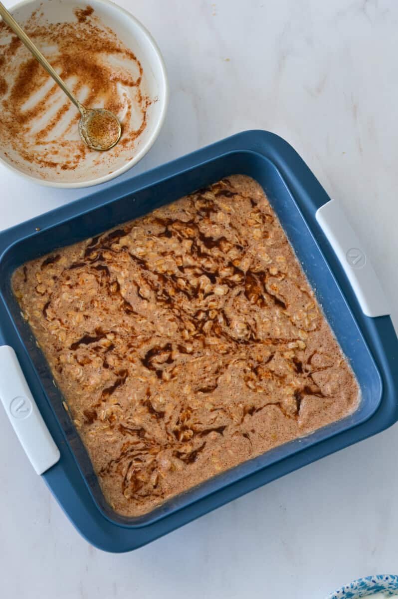 Baked oat batter added to a baking dish with cinnamon swirl.