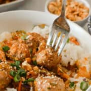 Fork lifting up a bite of the Asian chicken meatball served over rice.