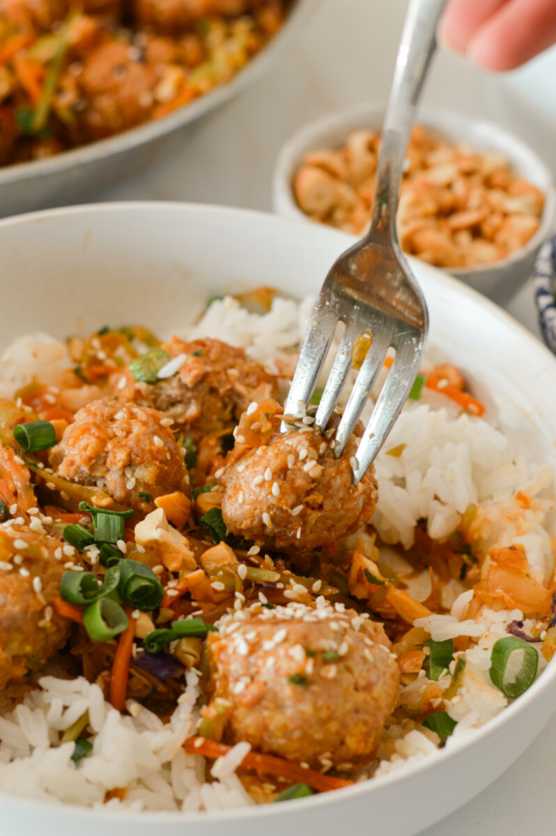 Fork lifting up a bite of the Asian chicken meatball served over rice.